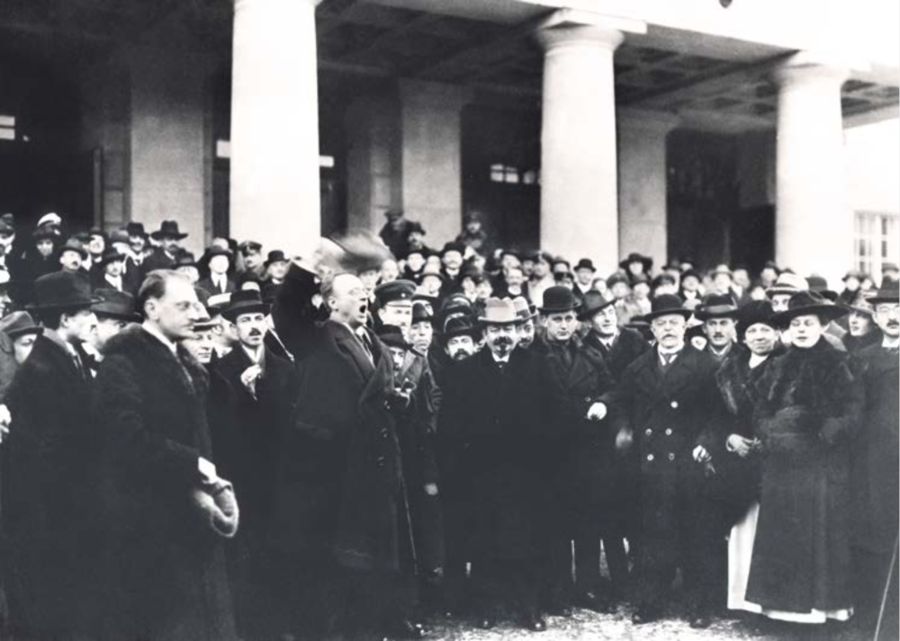 Adolf Köster (1883–1930) waving his hat and cheering up the crowd to bring out three hurrahs for the very first democratic head of state in German history, Friedrich Ebert. In the background the theatre building of Weimar.