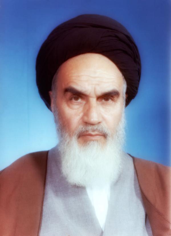 A portrait of a man with a mid-length white beard and black head covering, staring forward intently.